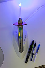 Ein Instrument zur Aushärtung von Füllungen steht in einem abgedunkelten Raum auf dem Tisch, das bläuliche UV-Licht ist zu sehen