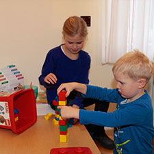 Zwei Kinder sitzen an einem kleinen Holztisch im Wartezimmer und spielen mit Lego-Duplo-Bausteinen