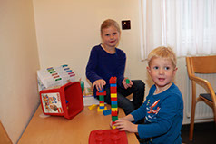 Zwei Kinder sitzen an einem kleinen Tisch im Wartezimmer, auf dem Tisch liegen Lego-Duplo-Bausteine